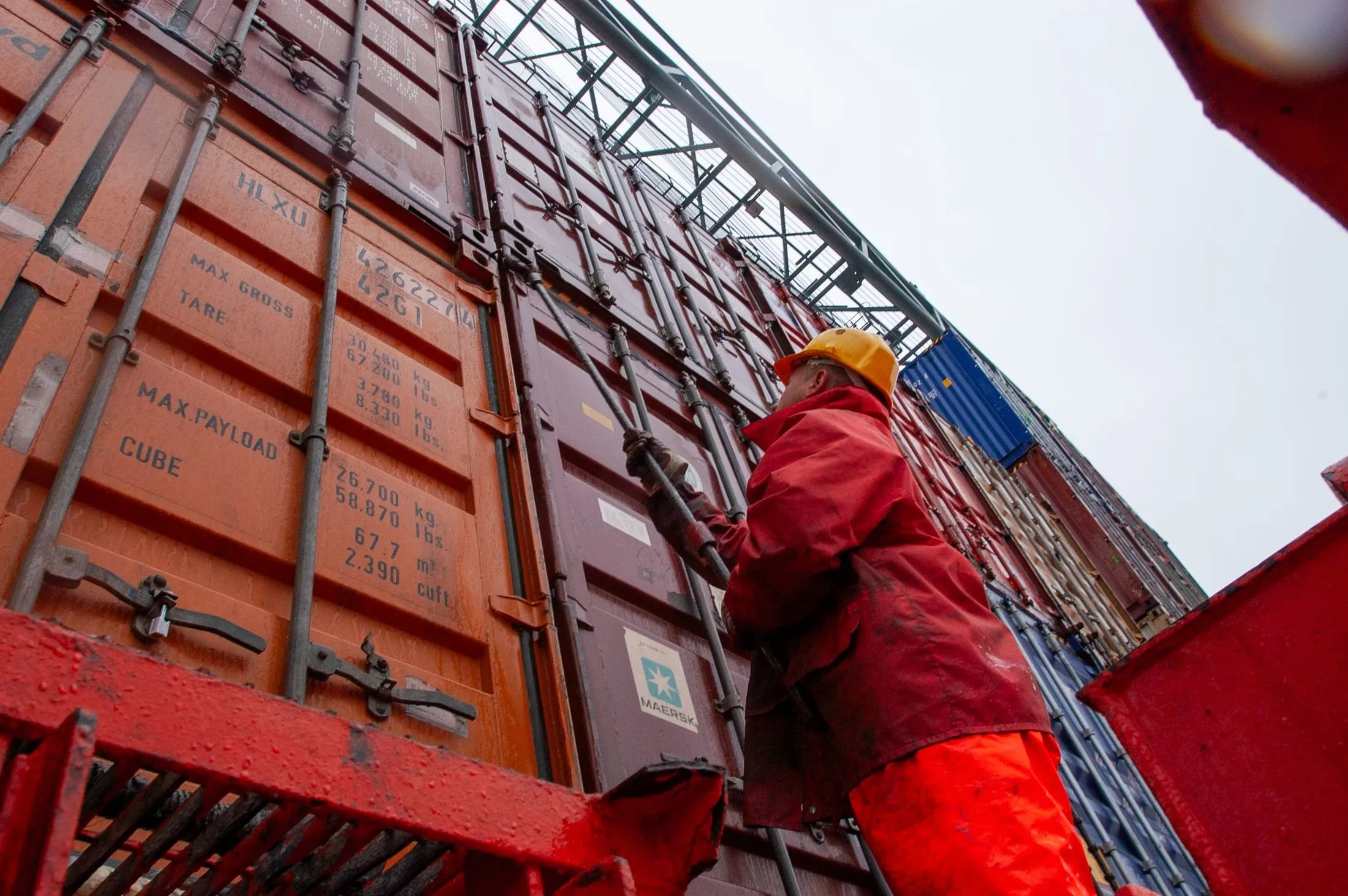 Port worker in a hard hat checking a container door on the quay