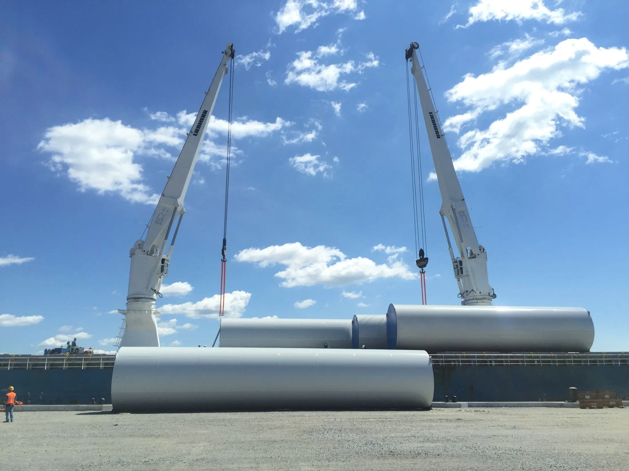 Two port cranes lifting large steel cylinders on a quayside